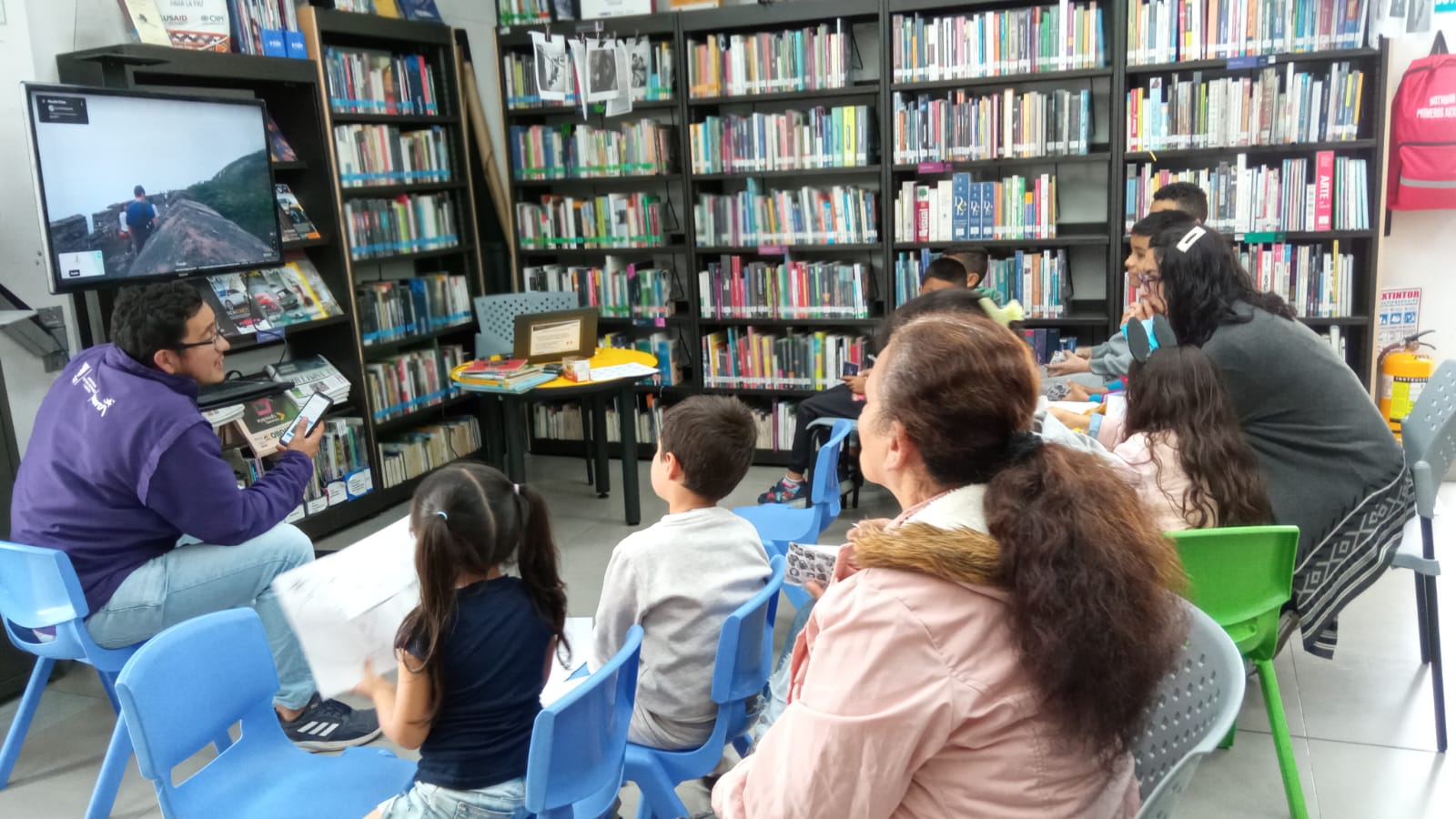 niñas, niños y mamás viendo una película en la biblioteca