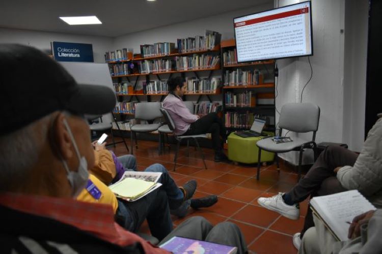 Personas reunidas en una biblioteca viendo una presentación en el televisor