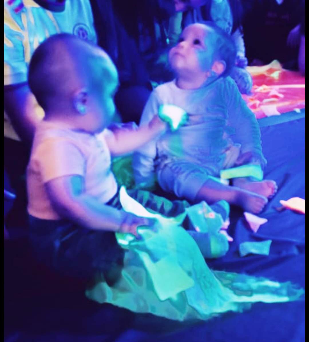 dos bebés jugando con colores neón en un cuarto con luz azul