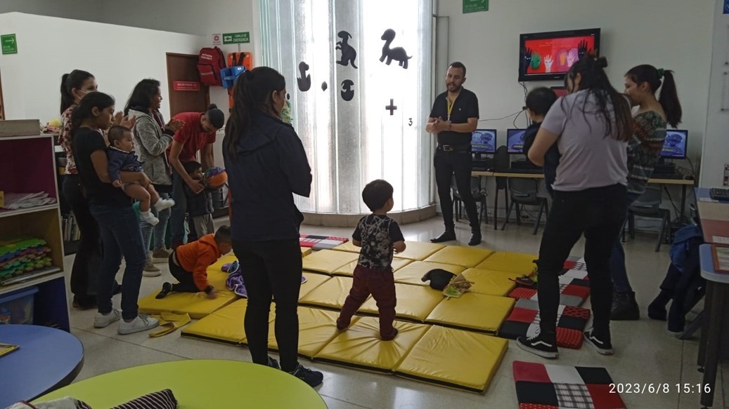 grupo de bebés junto a sus cuidadores en medio de un taller realizando actividad física.