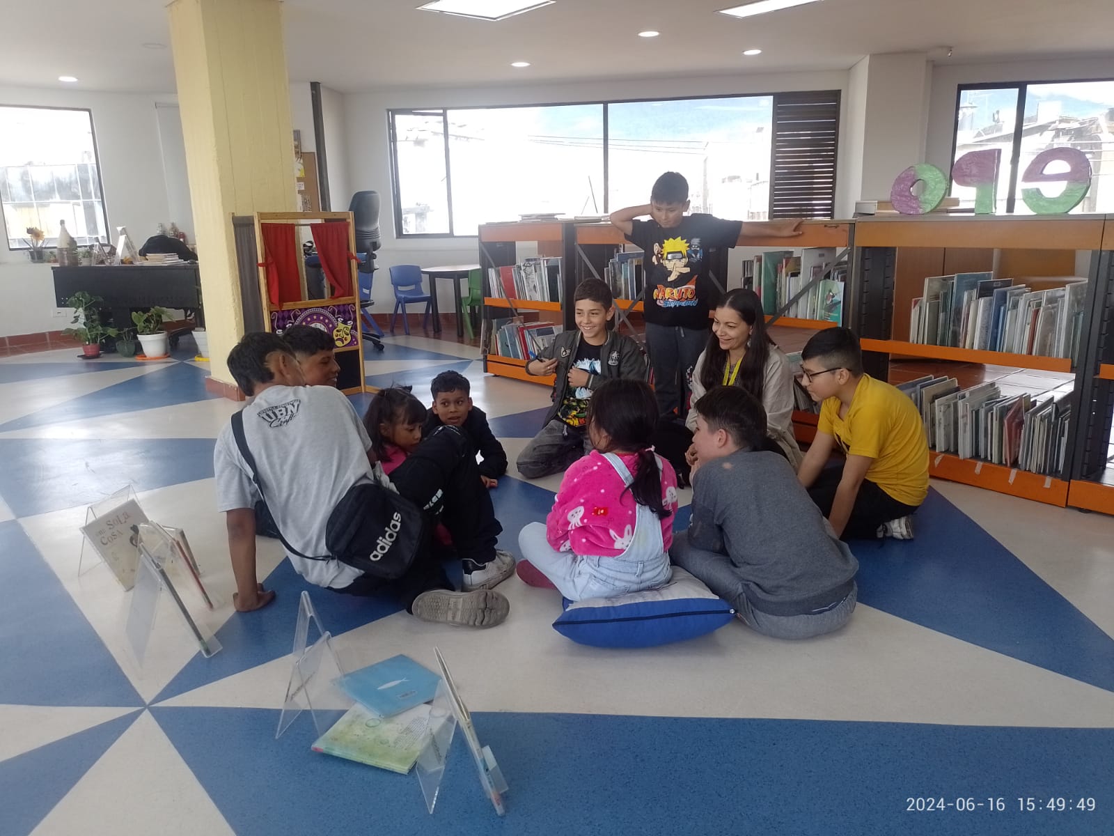 grupo de niños sentados en círculo en el suelo junto a su docente mientras leen 