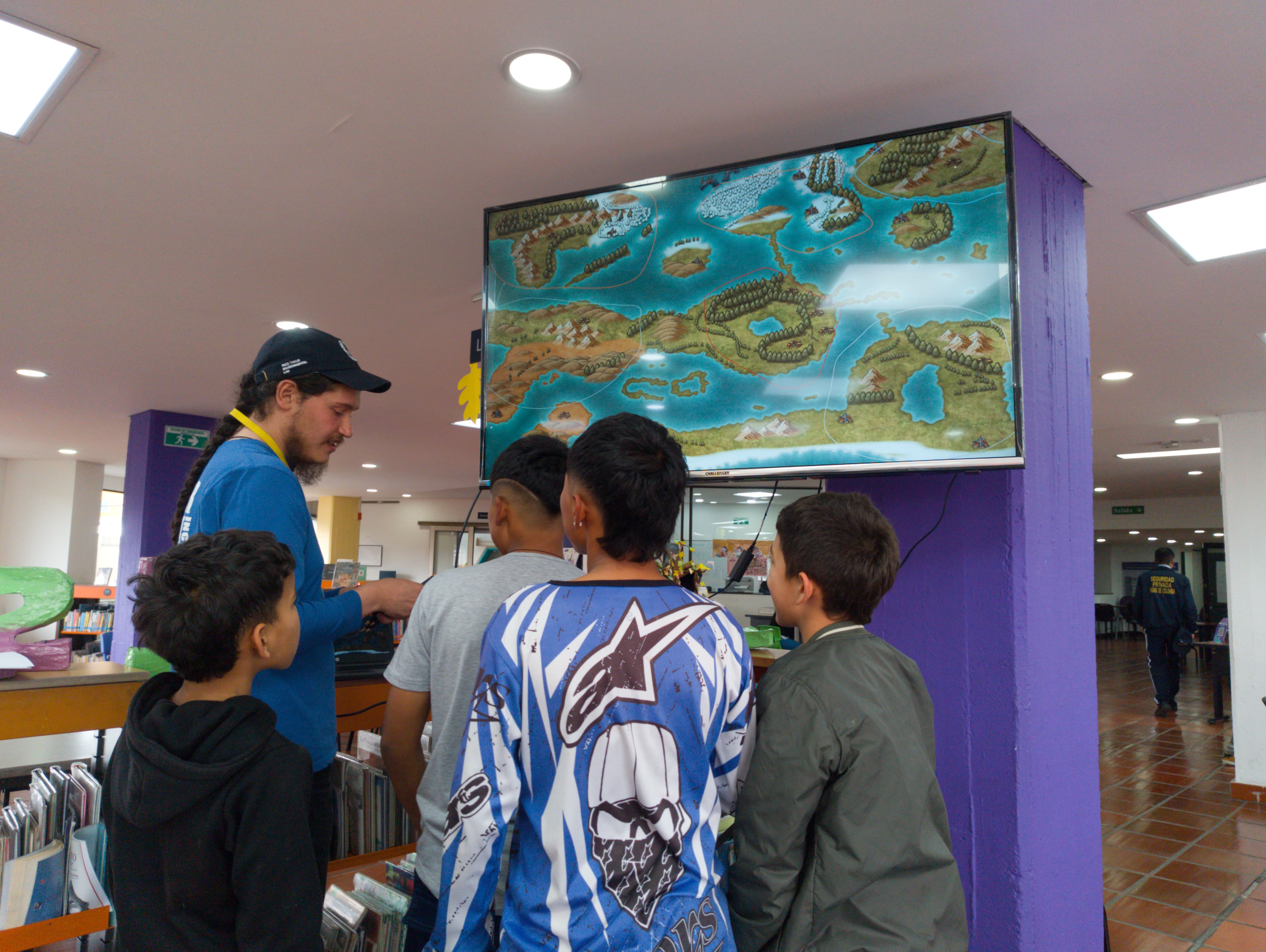 Grupo de niños frente a un televisor mientras un docente les explica el funcionamiento de un video juego.