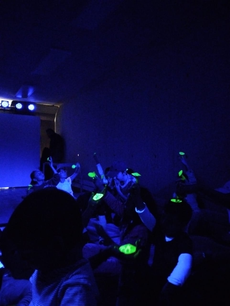 un grupo de niñas y niños jugando con luces neón en medio de un cuarto con luz azul
