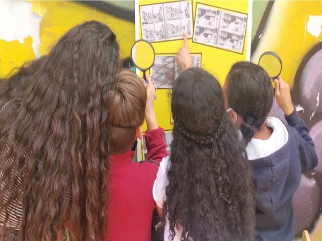 niños y niñas observando y analizando varias imágenes mientras ubican objetos con lupas.