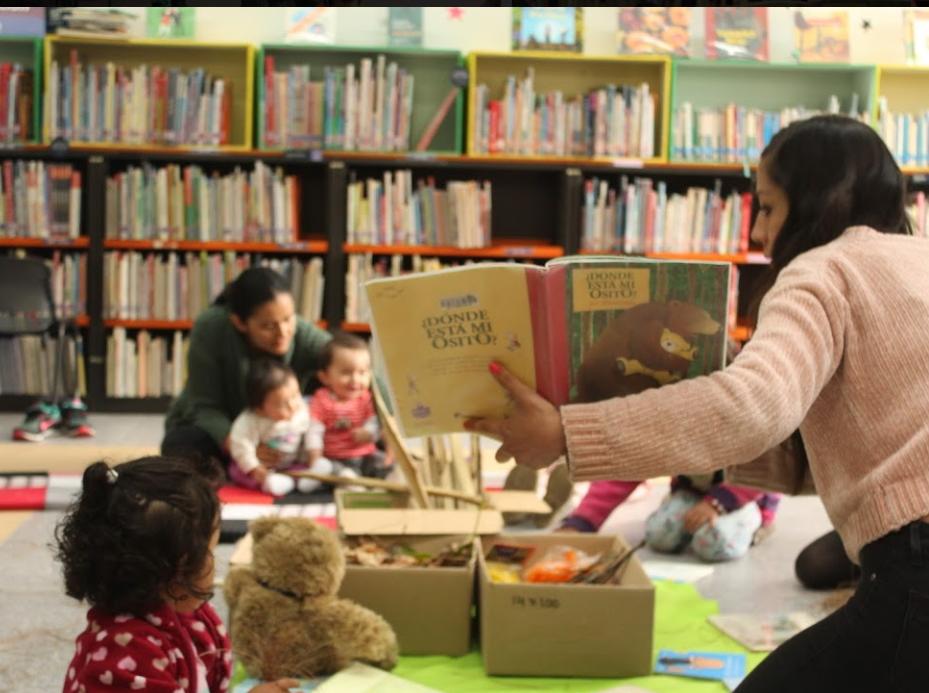 Cuidadores con sus bebés participando en actividades para la primera infancia en la sala infantil de la biblioteca