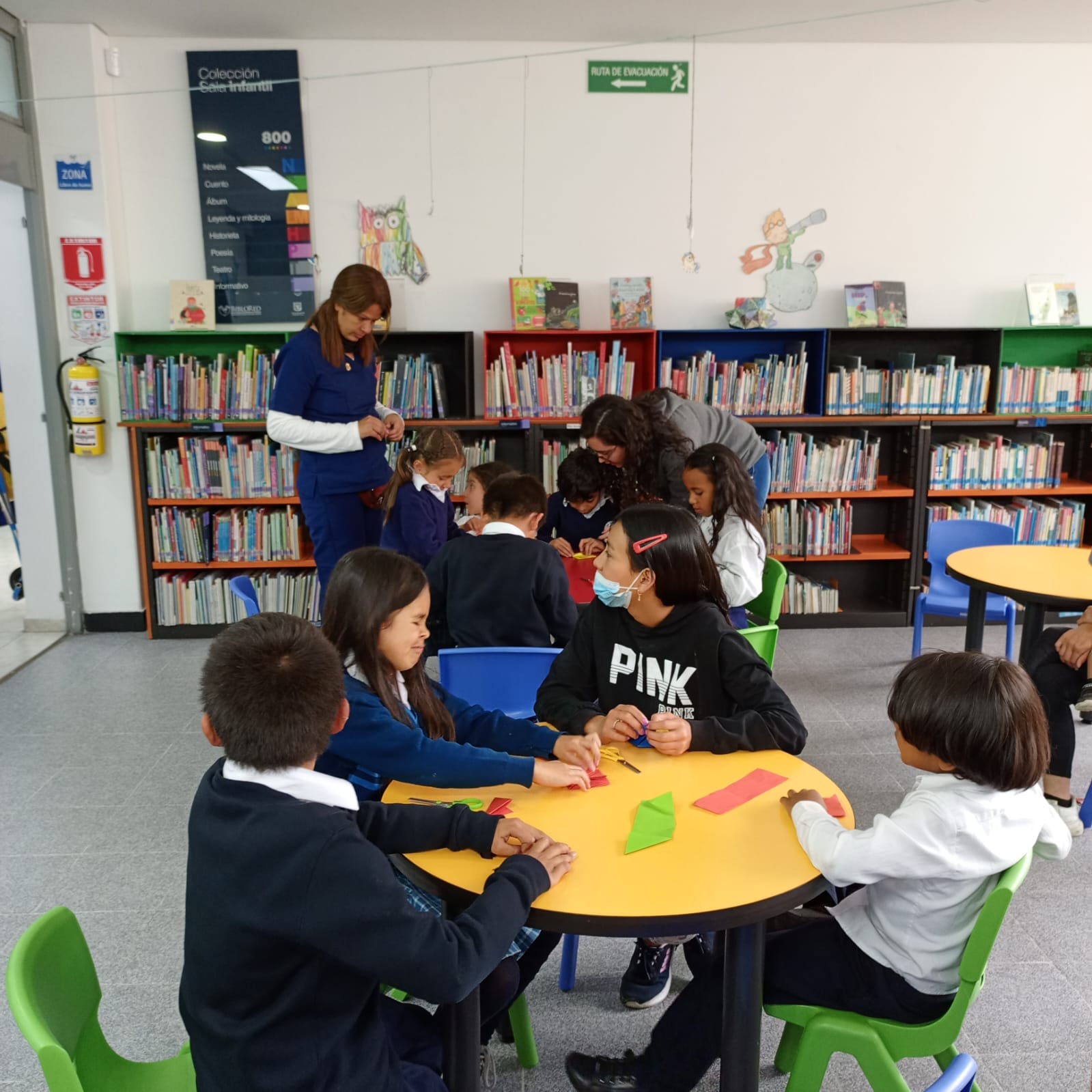 grupo de niños sentados al rededor de mesas de colores en medio de un taller de manualidades