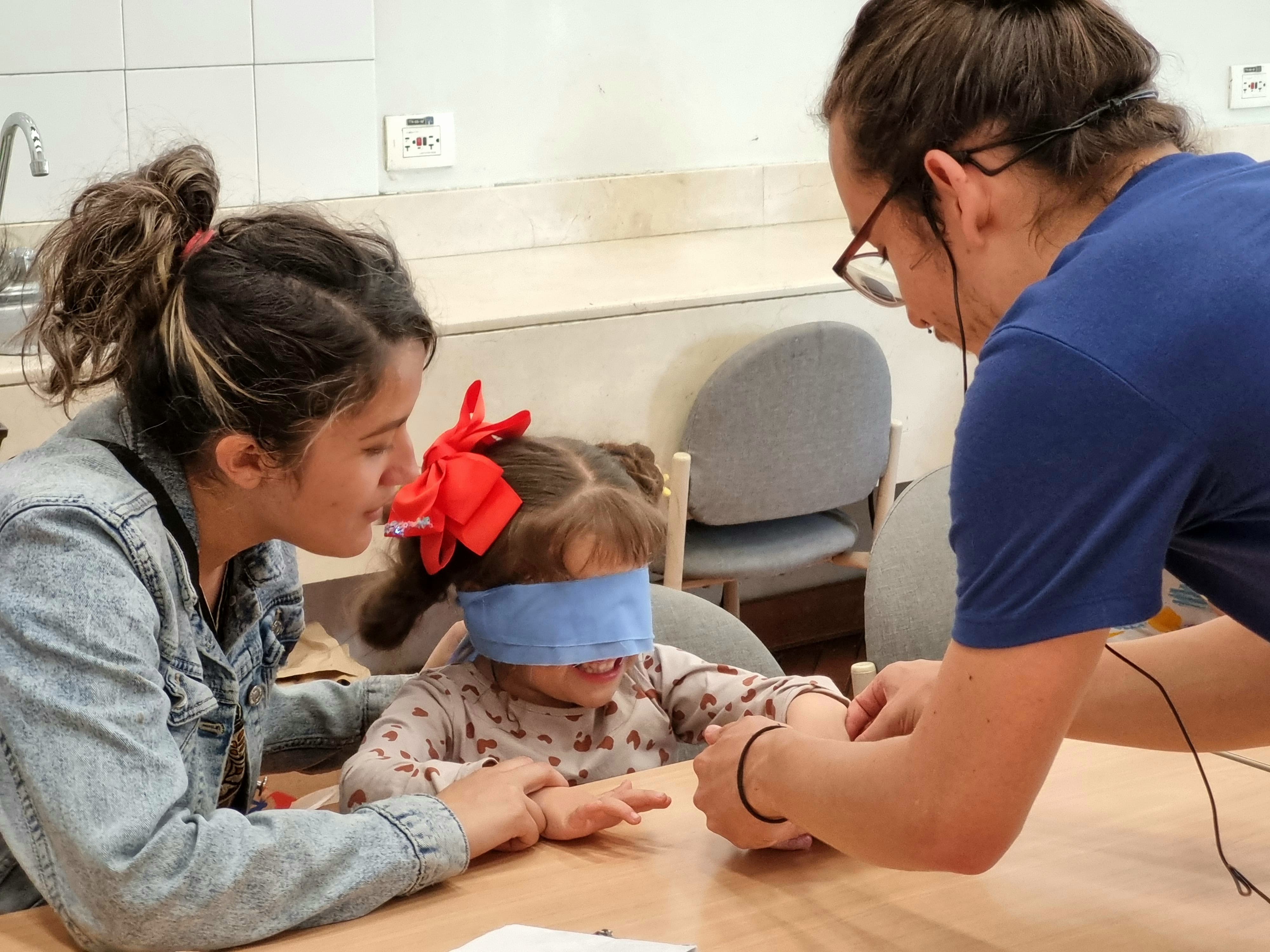 una niña con los ojos vendados interactuando con el docente y su madre