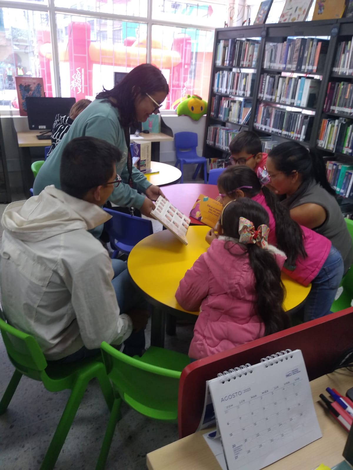 grupo de niños y niñas prestando atención al libro que les muestra el docente