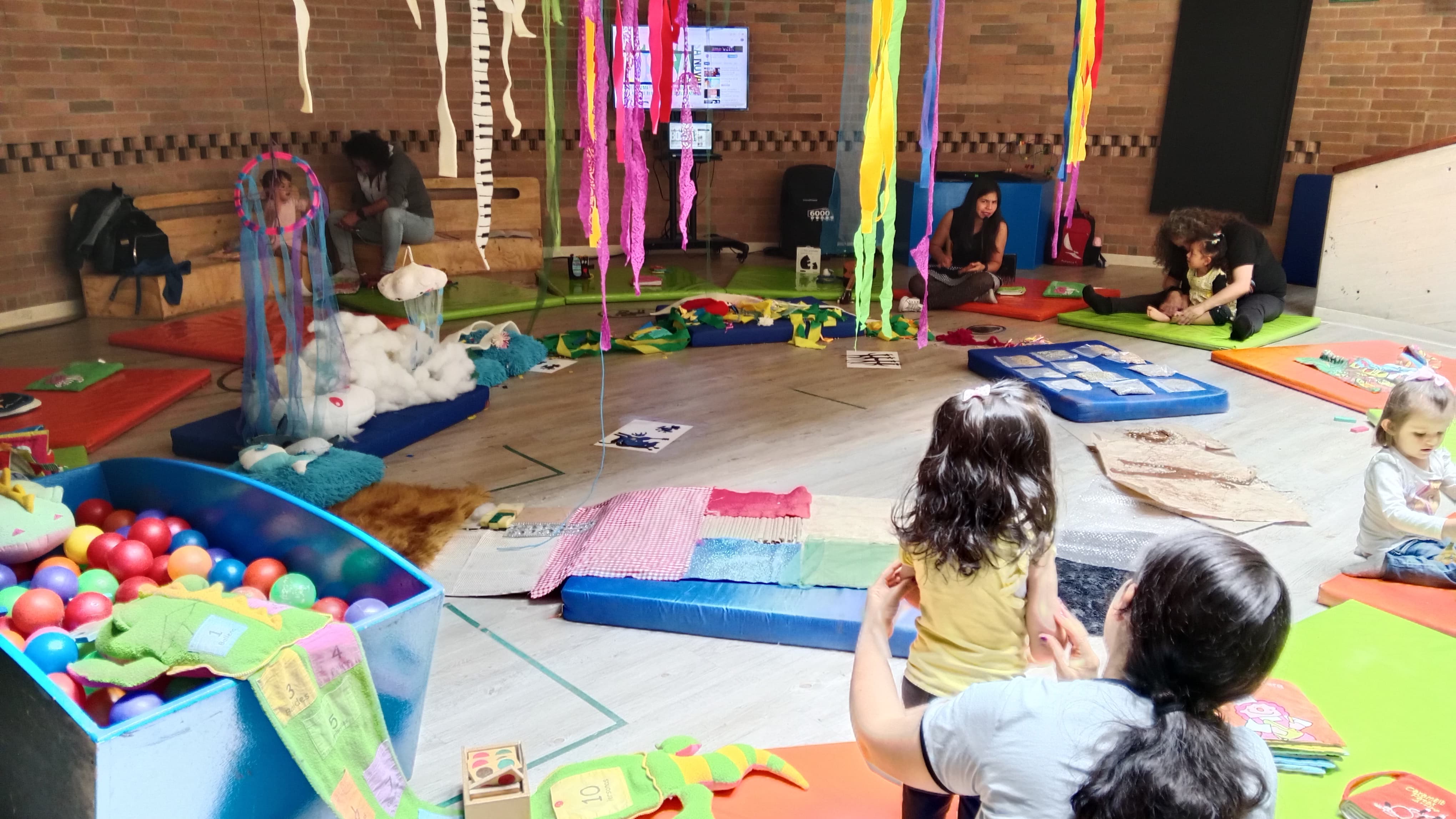 grupo de niños jugando en medio de un salón con tiras de papel de colores colgadas al techo