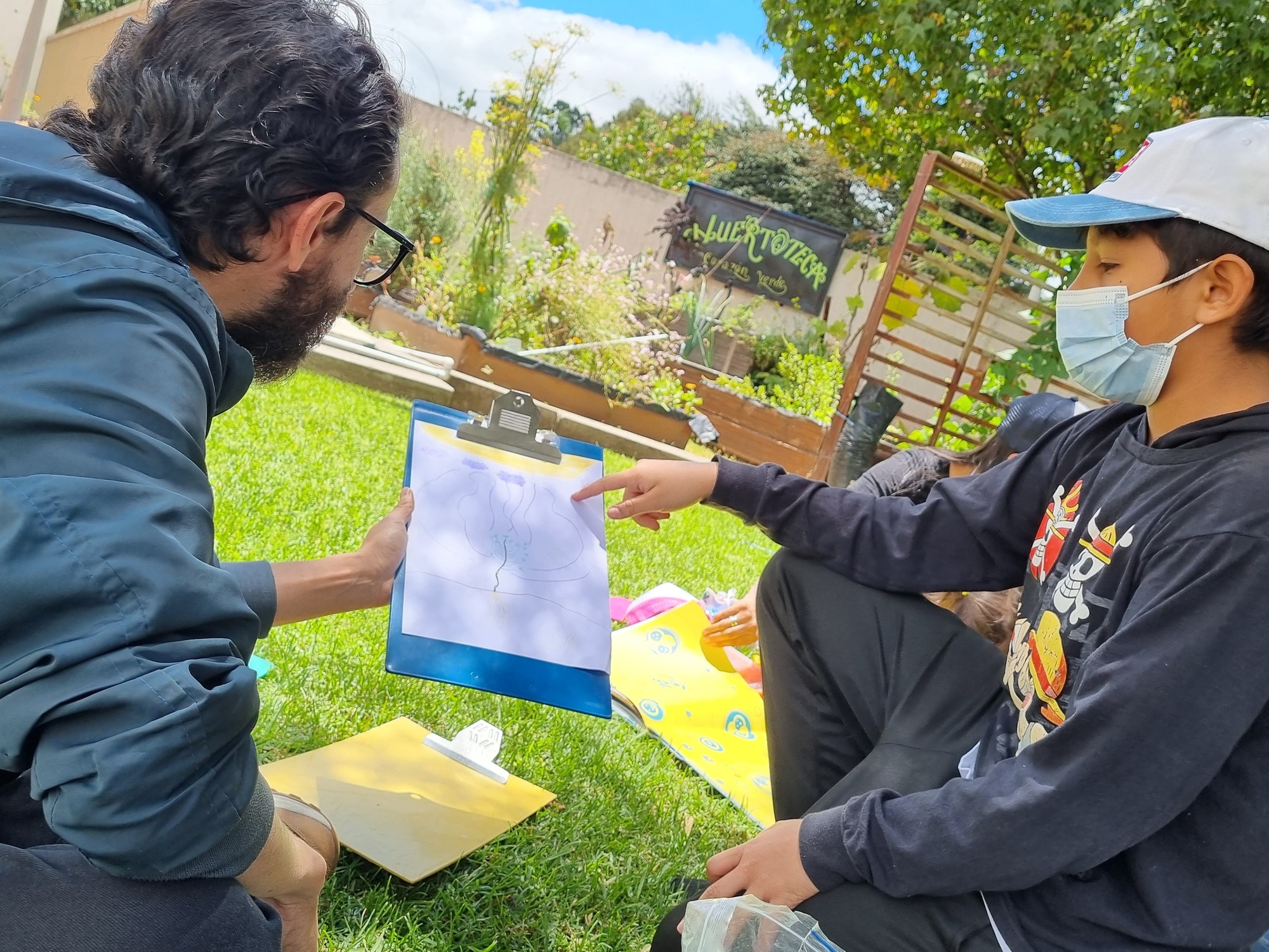 niño señalando el dibujo que hizo mientras se lo explica al docente 