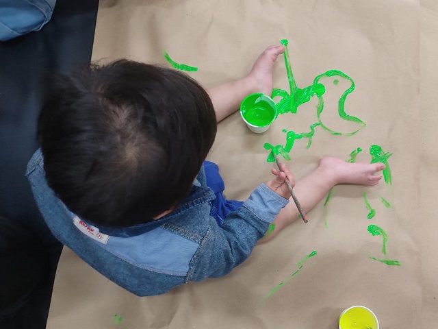 Bebe sobre papel kratf sobre el que esta pintando con un pincel y pintura verde