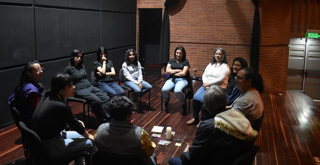 grupo de mujeres sentadas en círculo en la tarima de un teatro 