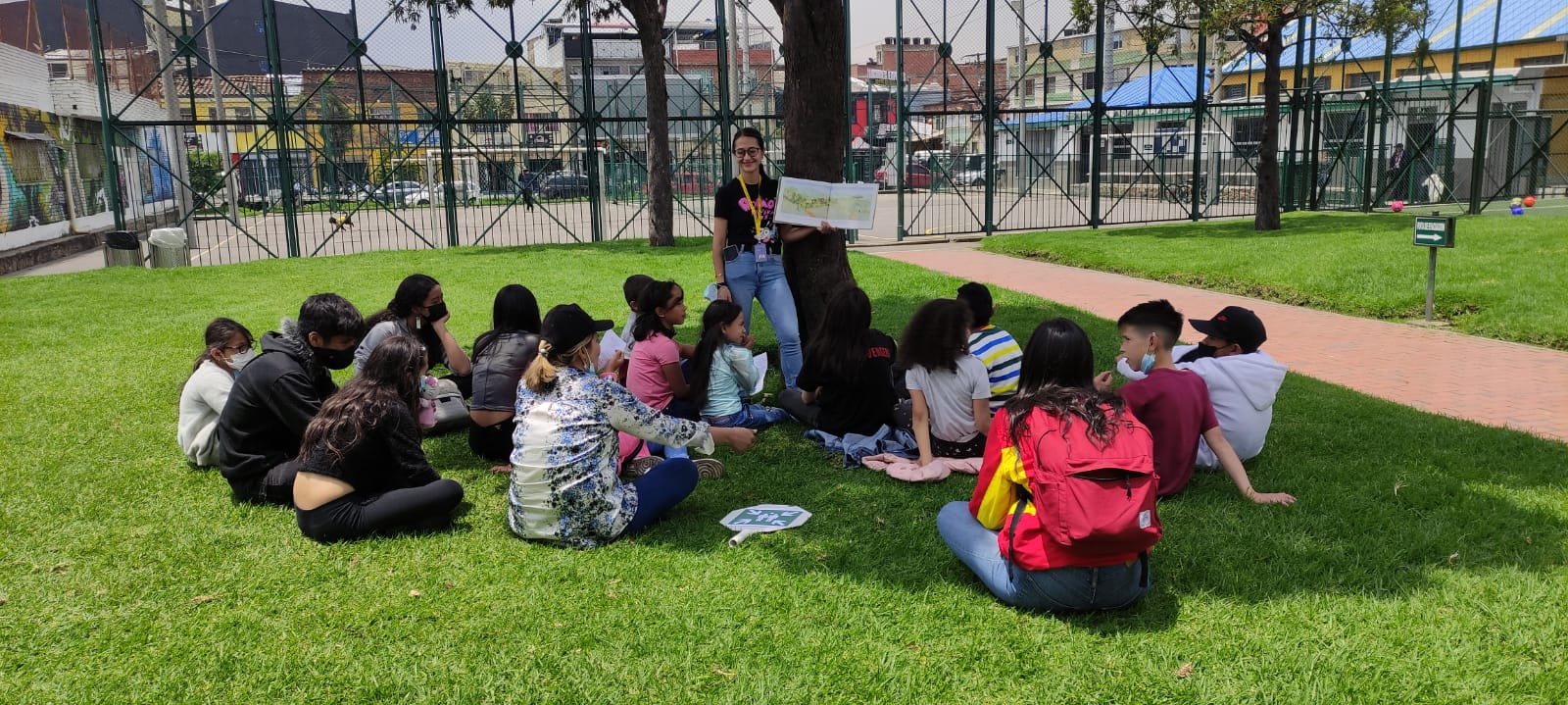 grupo de niñas y niños leyendo al aire libre bajo la sombra de un árbol 