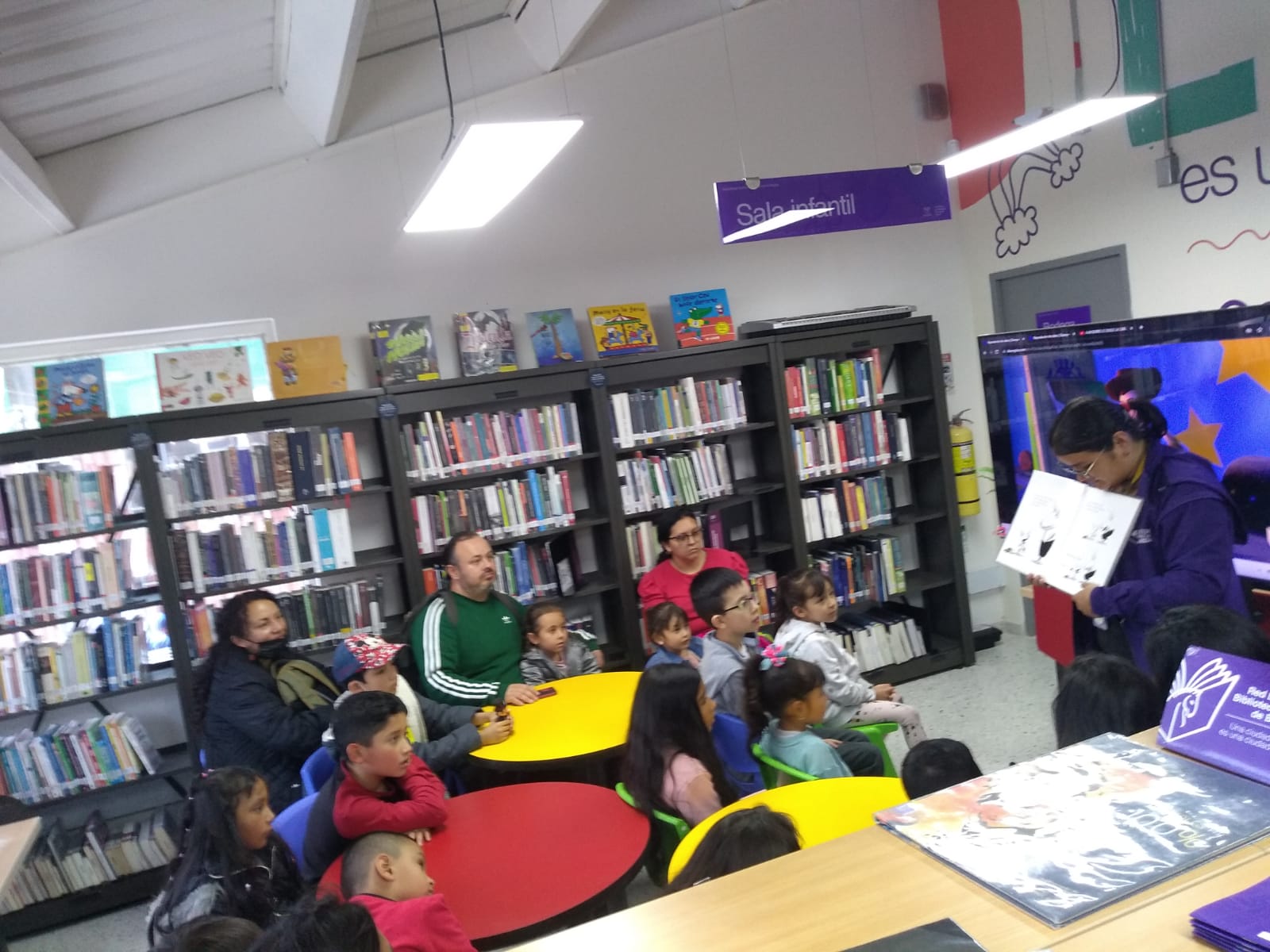 Infancia junto a sus cuidadores participando en el club de lectura infantil en la biblioteca