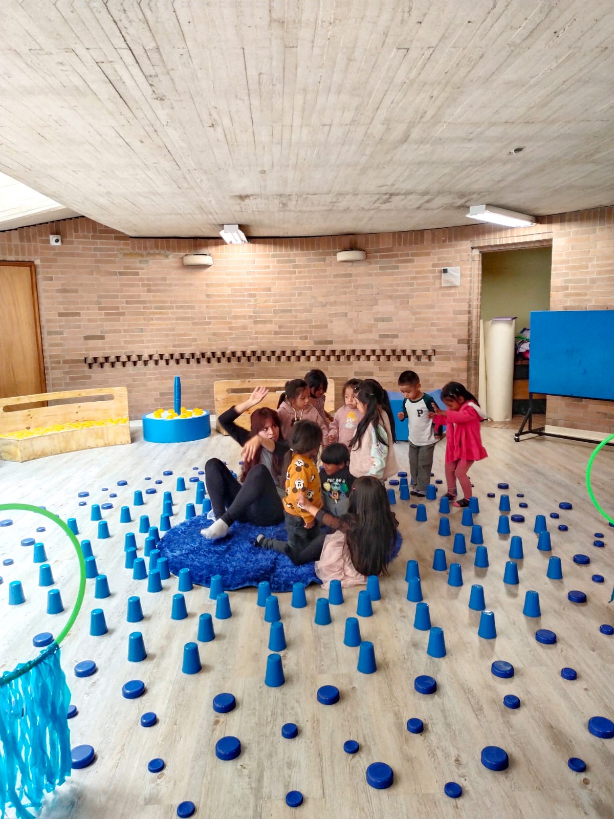 grupo de niños y niñas jugando en medio de un salón con vasos de color azul 