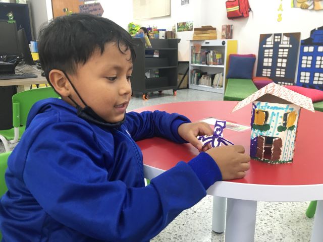 niño jugando con una casa y un muñeco realizados por él en papel 