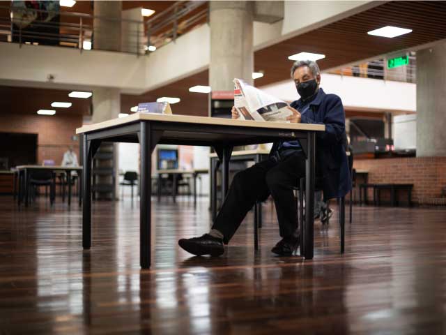 Adulto mayor leyendo un libro en la sala general de la biblioteca