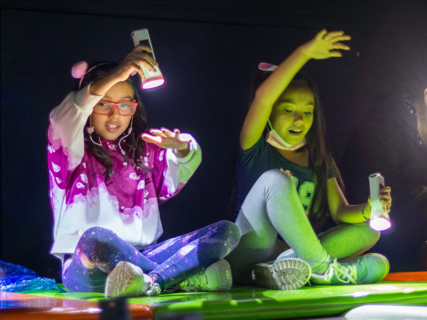 dos niñas jugando con la luz de una linterna haciendo sombras con sus manos