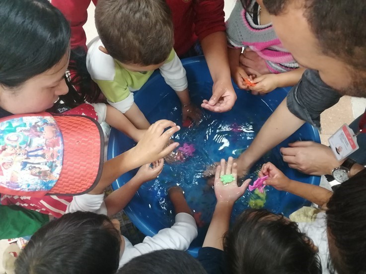 niños sacando juguetes de plástico de un balde con agua