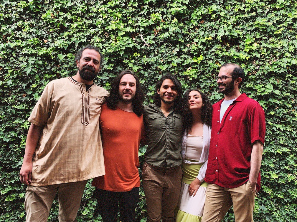 grupo de personas que consta de 4 hombres y 1 mujer al frente de unos árboles posando para la foto abrazados