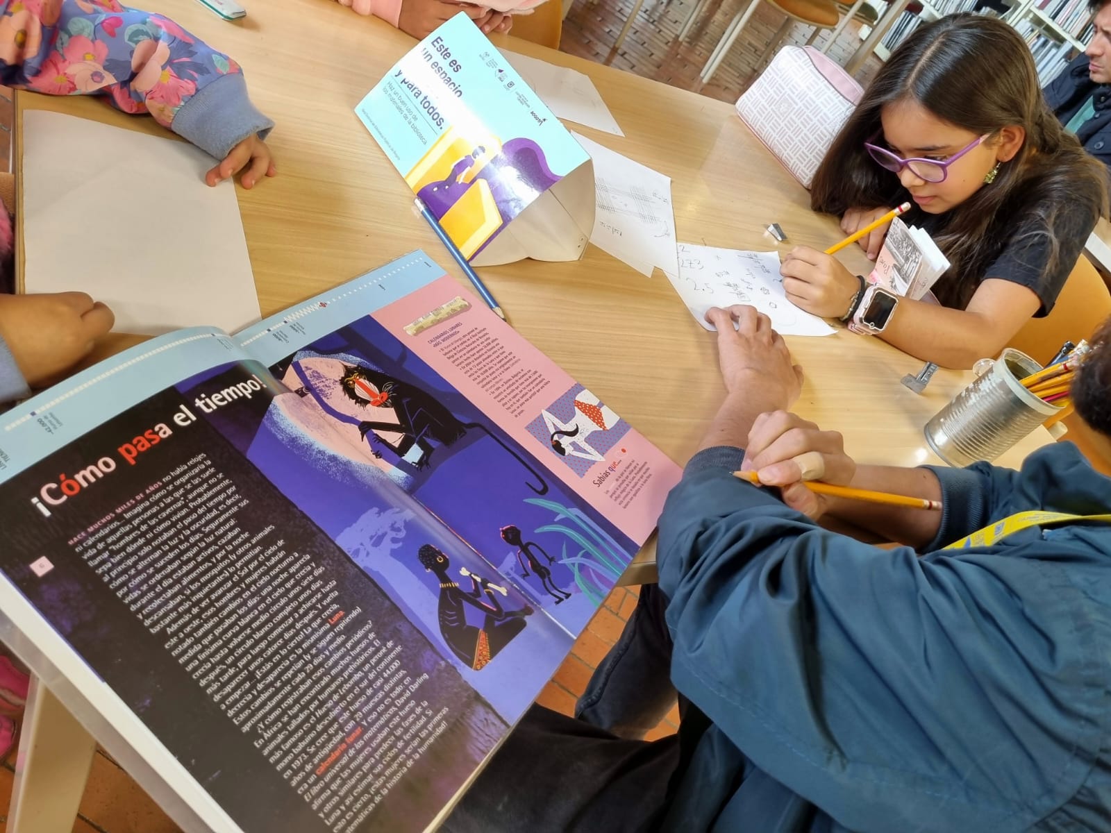 una niña escribiendo sobre un papel blanco con un libro abierto a su lado