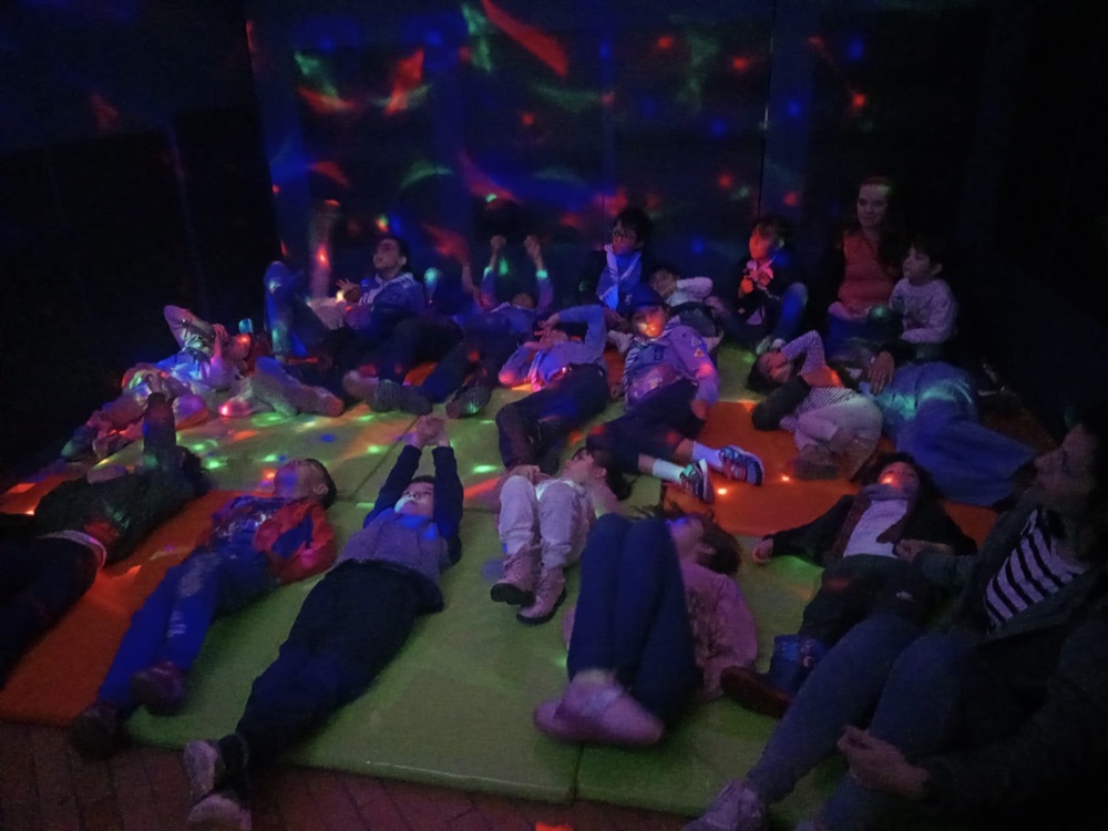 grupo de niñas y niños en medio de un salón con luz azul y pintura neón