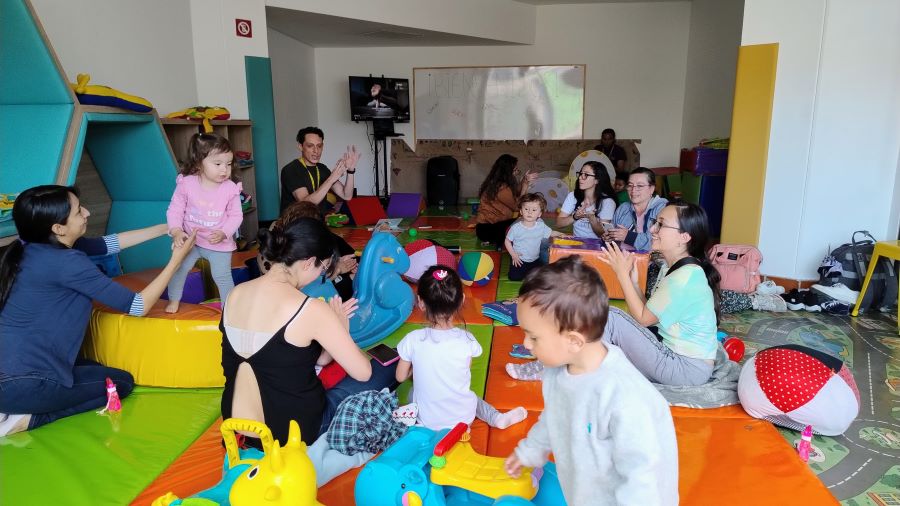 grupo de niños y niñas acompañados de sus padres jugando en la bebeteca de una biblioteca 