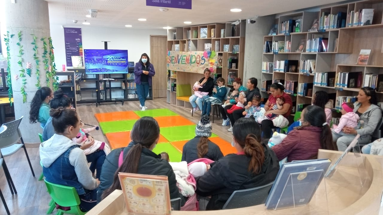 grupo de mujeres con sus bebés de brazos prestando atención a la docente