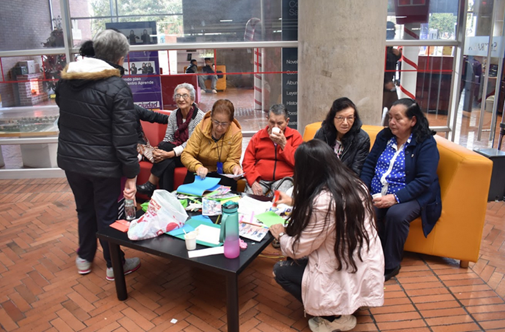 grupo de adultos mayores sentados en un sofá color rojo mientras conversan