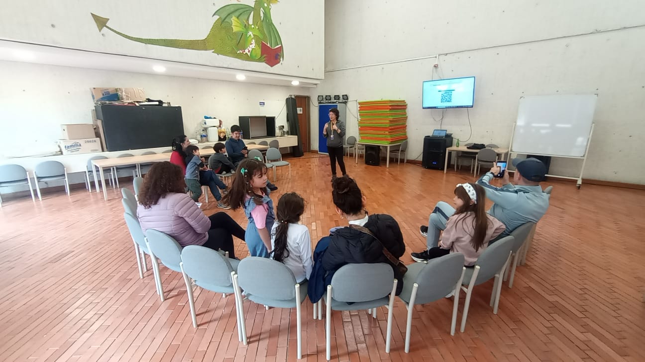 Teatro para la infancia grupo de niños, niñas junto a sus padres escuchando a la docente dando una instrucción